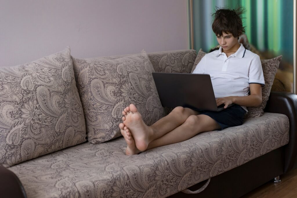Подросток пользуется ноутбуком, отдыхая на диване
