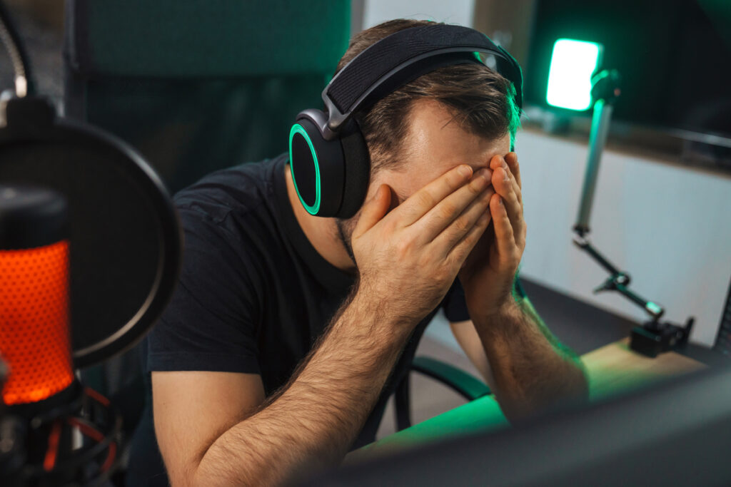 Расстроенный мужчина в наушниках закрывает лицо руками