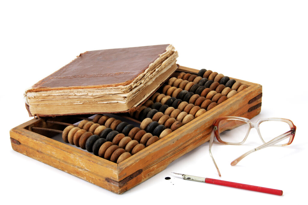 Старая книга, лежащая на бухгалтерских счётах, рядом с пунктами и ручкой
