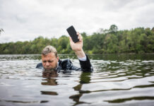 Если смартфон намок: пошаговое руководство к действию Бизнесмен держит мобильный телефон в озере