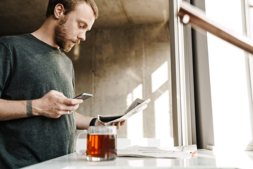 Мужчина держит в руках газету и телефон