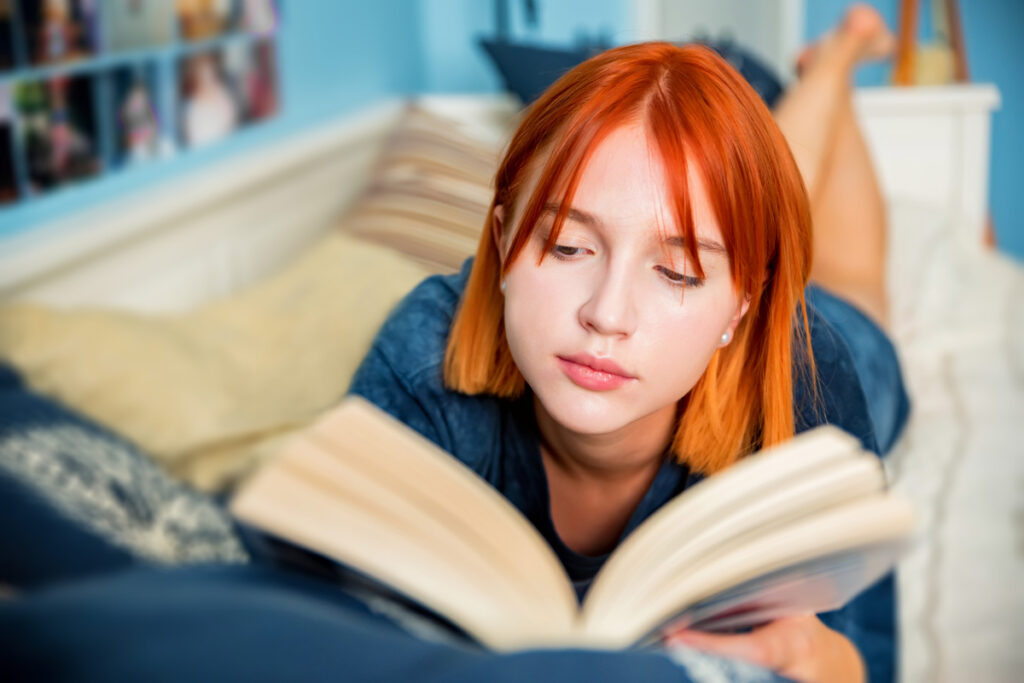 Девушка-подросток читает книгу лёжа