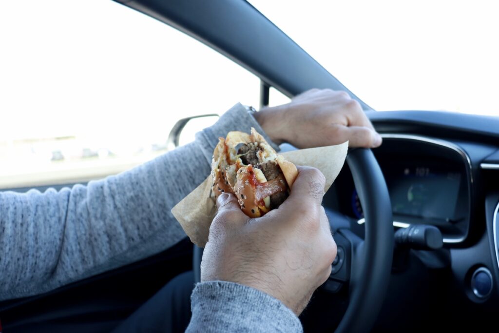Мужчина ест гамбургер за рулём