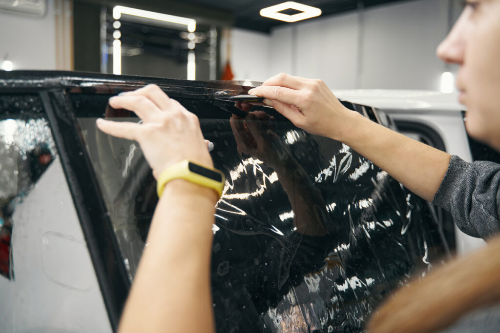 Работник обрезает тонированные пленку по краям