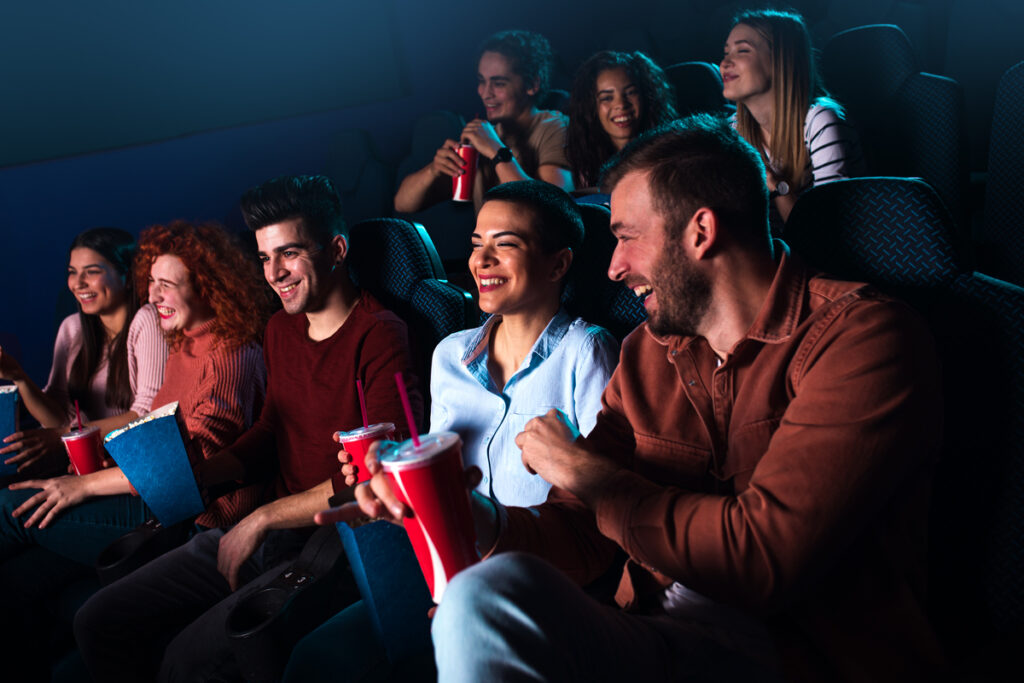 Группа весёлых людей смеётся, смотря фильм в кинотеатре