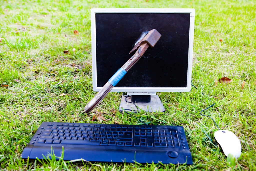 Разбитый молотком компьютерный монитор на зеленой траве