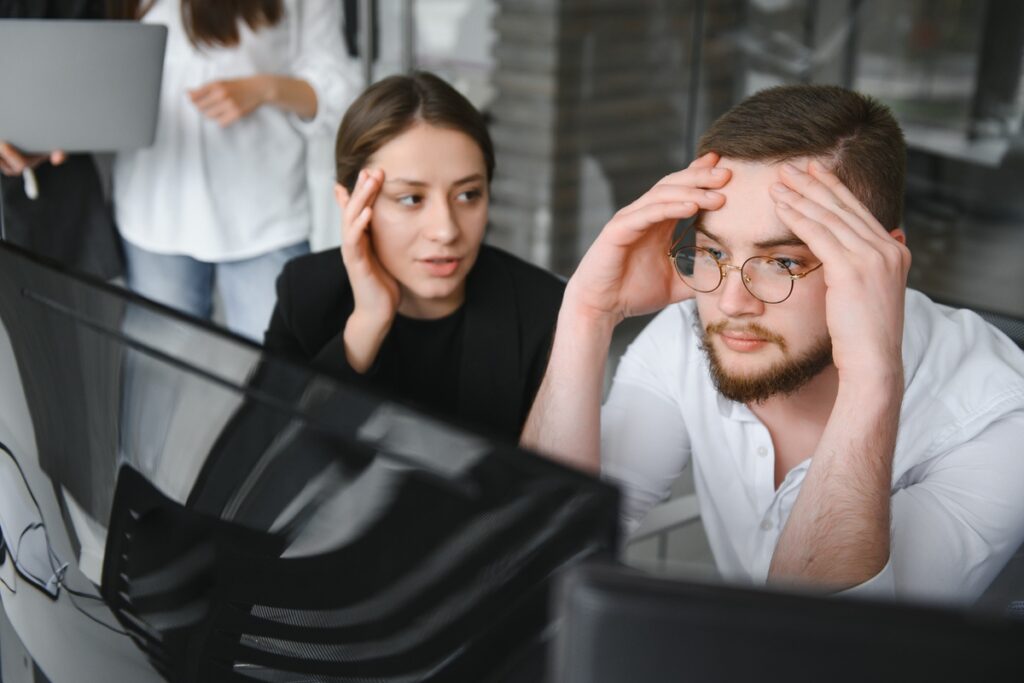 Женщина и мужчина, сидящие перед компьютерами и испытывающие стресс