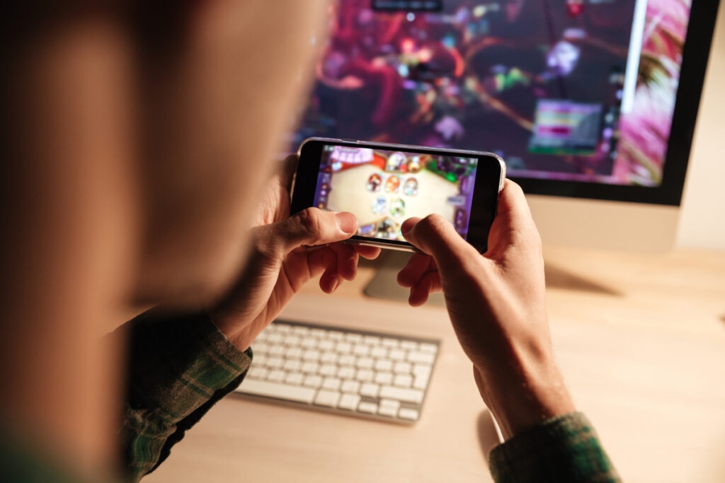 Взрослый играет в мобильную игру за компьютерным столом