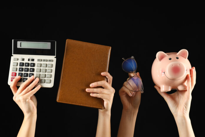 руки держат калькулятор, блокнот, очки и копилку