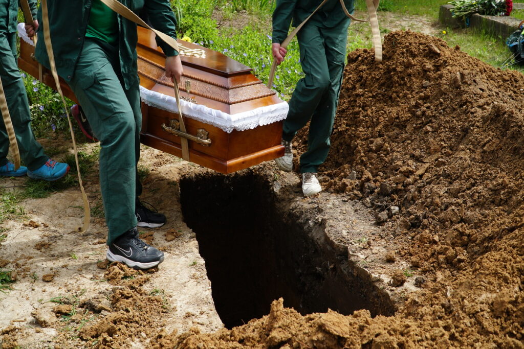 Мужчины опускают гроб в могилу