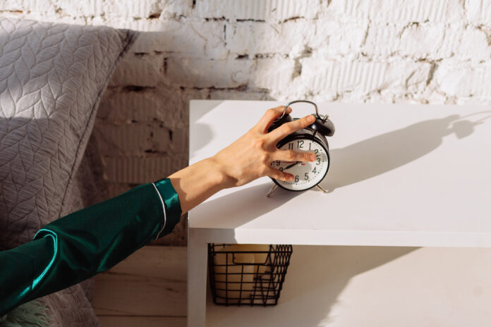 Рука тянется выключить будильник