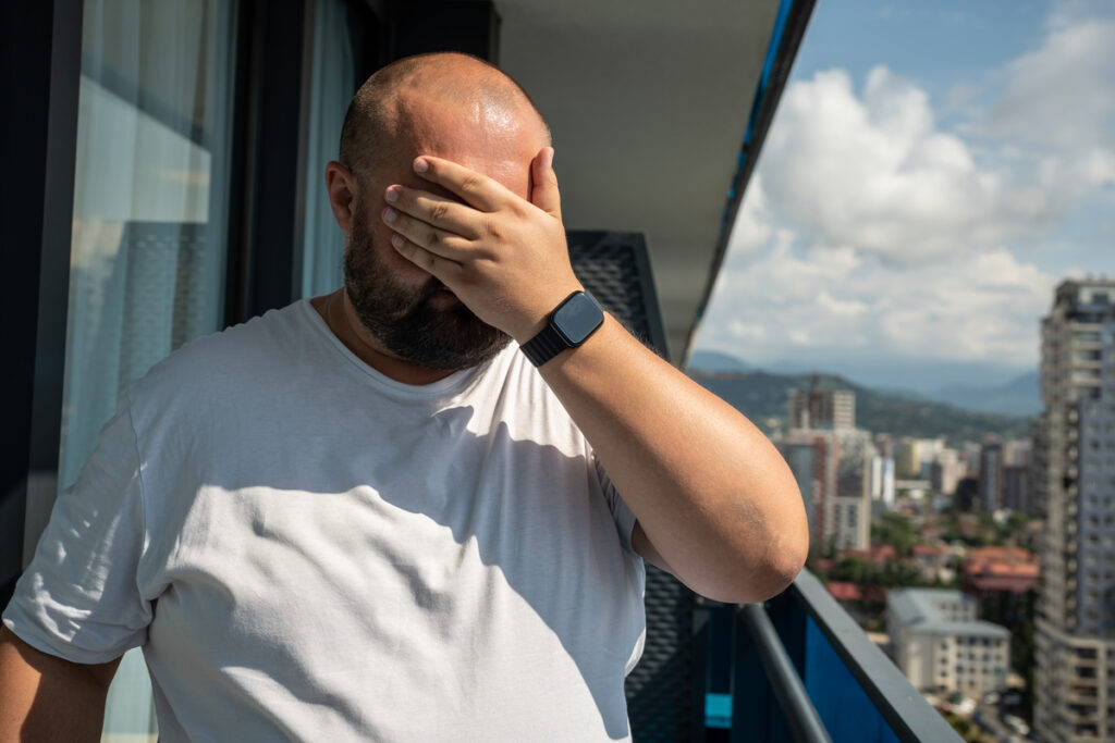 Мужчина закрывает лицо рукой
