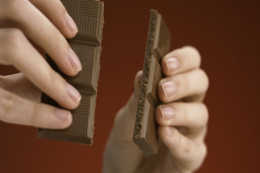 Крупный план рук, разбивающих плитку шоколада на две части