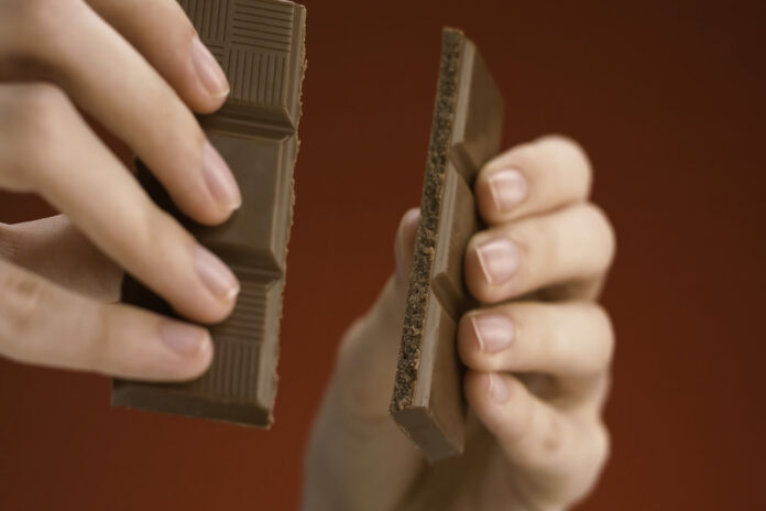 Крупный план рук, разбивающих плитку шоколада на две части