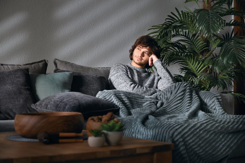 Молодой человек сидит на диване под пледом