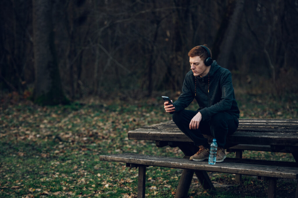 Молодой человек сидит в телефоне на улице