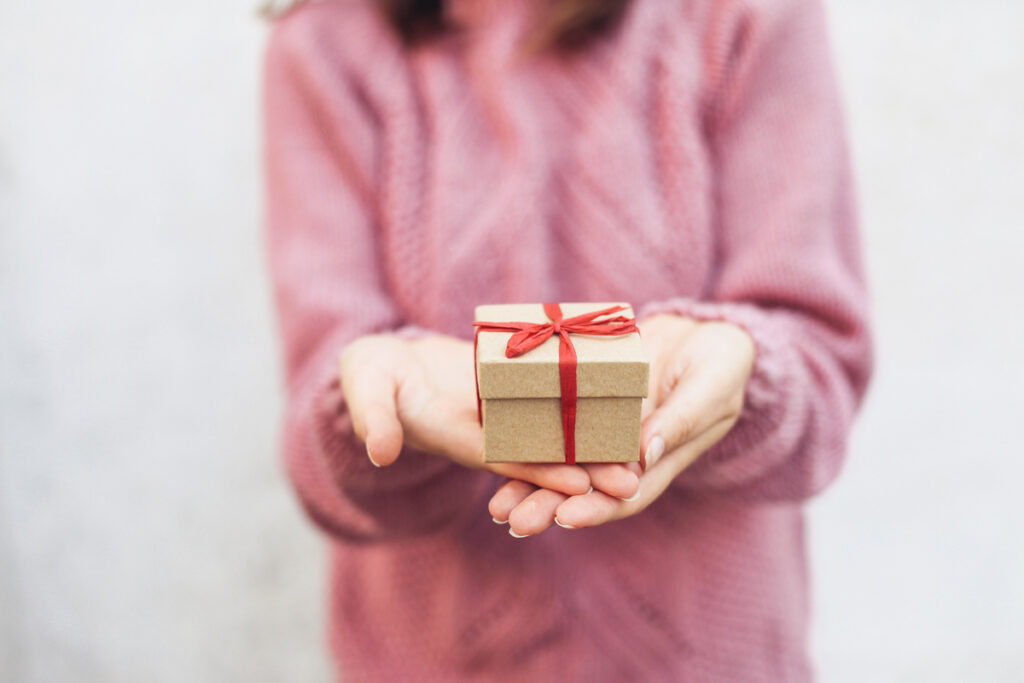 Маленькая подарочная коробка с красной лентой в женской руке