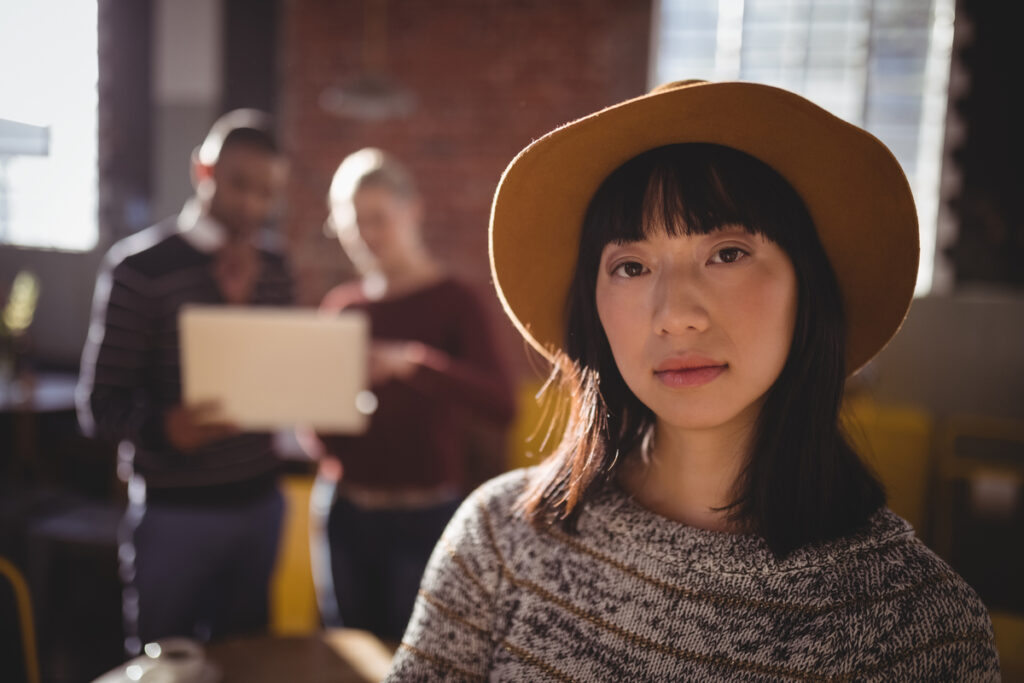 Portrait of confident young woman wearing hat while standing against colleagues - signaldaily молодая девушка