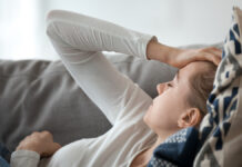 UpsetDepressedYoungWomanLyingOnCouchFeelingStrongHeadache