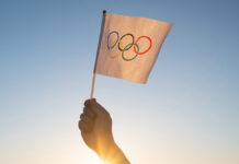 TheOlympicFlagSmallInHandFluttersAgainstTheBackdrop