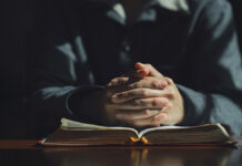 ChristianManHandsFoldedInPrayerOnHolyBibleIn