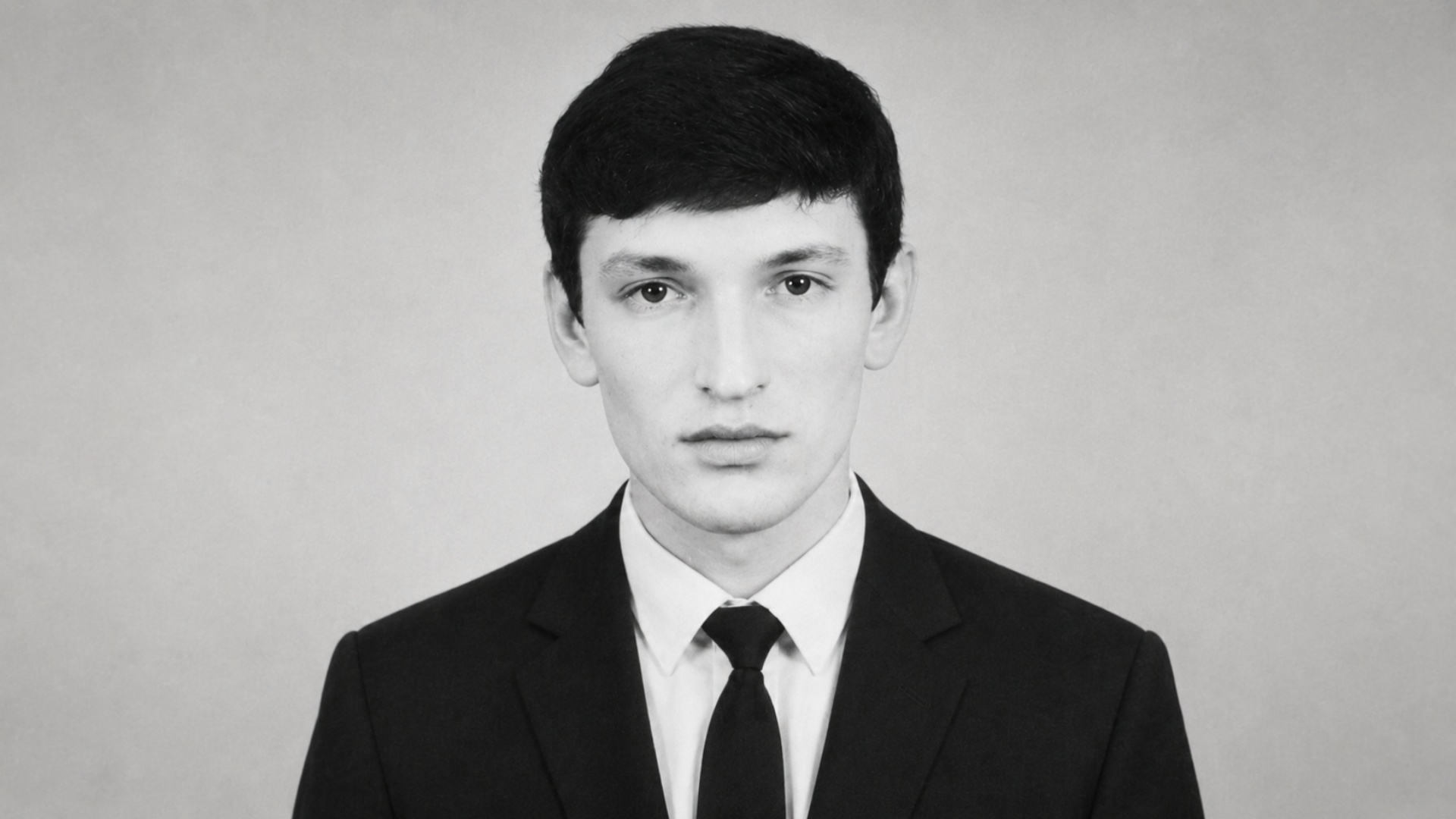 Black and white cinematic studio portrait of a man in a black classic suit, he slightly moves his...