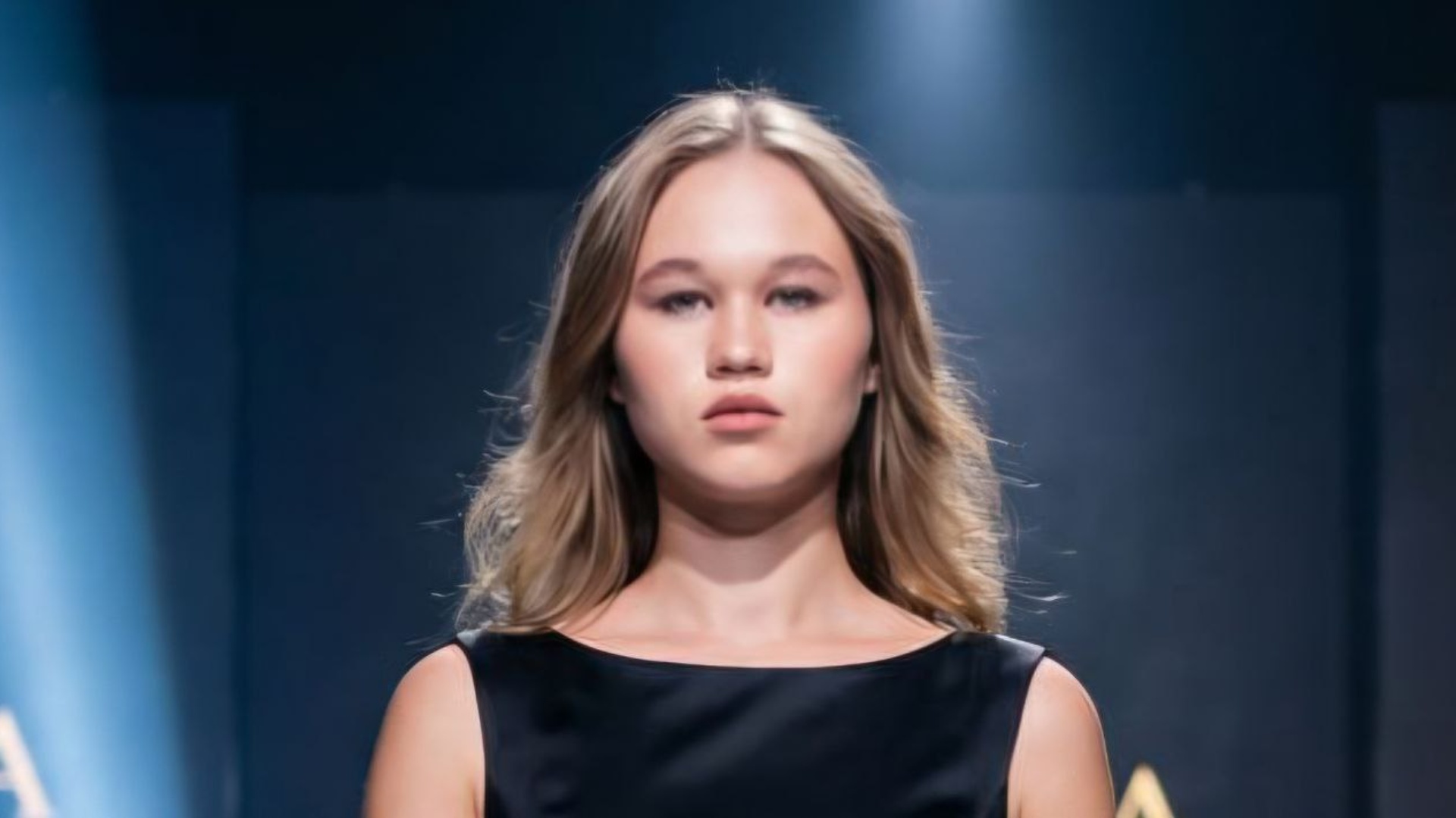Medium shot video of a stunning young woman walking on a fashion runway, framed from the waist up...