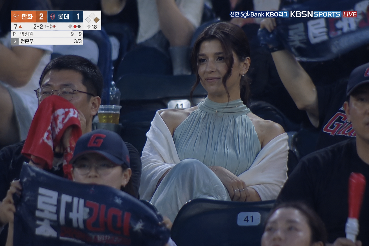 realistic sports broadcast screenshot-style documentary photo set in the spectator stands of a Ko...