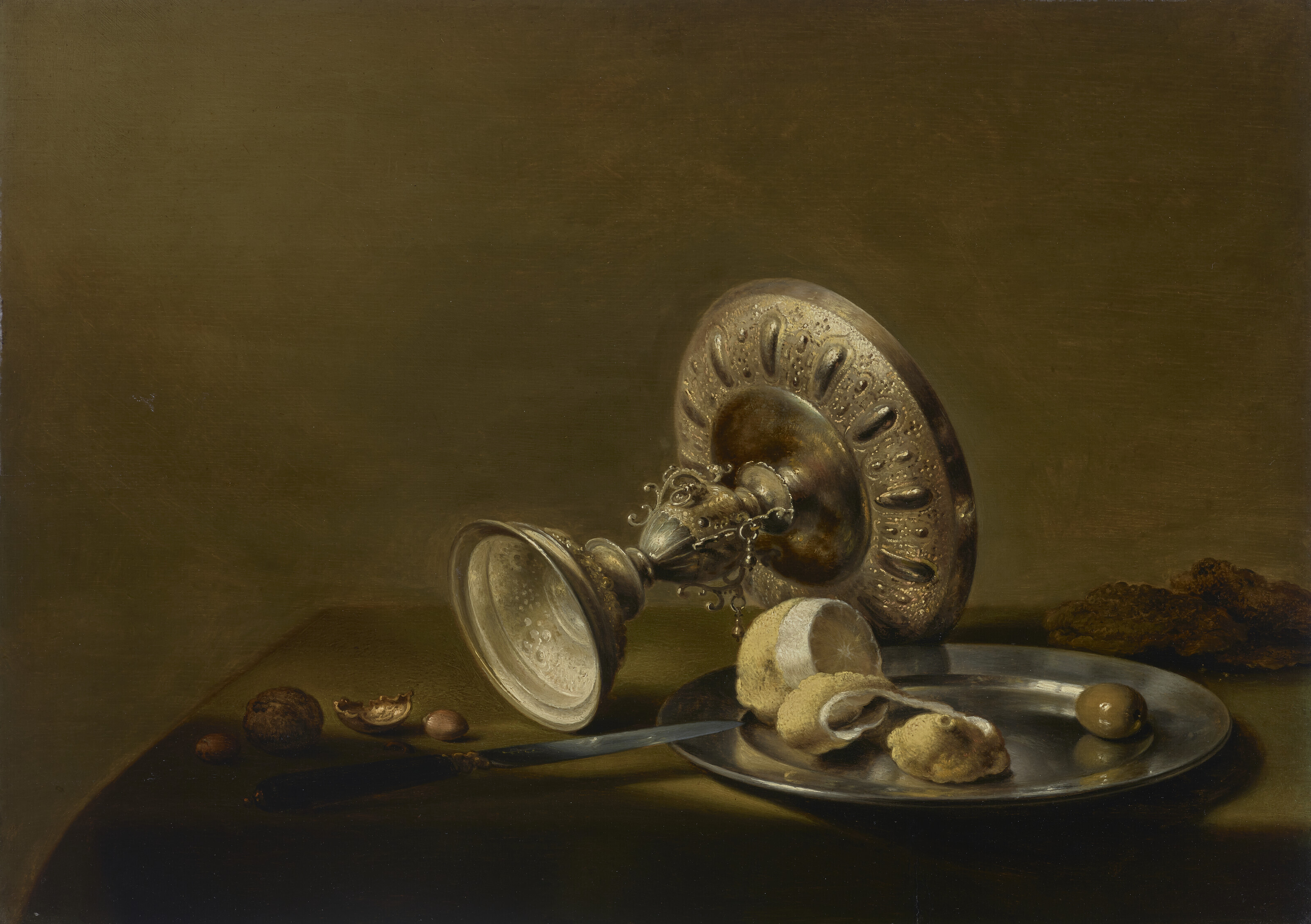 Pieter Claesz — Перевернутая серебряная тазца, частично очищенный лимон и оливка на серебряной тарелке, грецкие орехи, фундук и нож на задрапированном столе